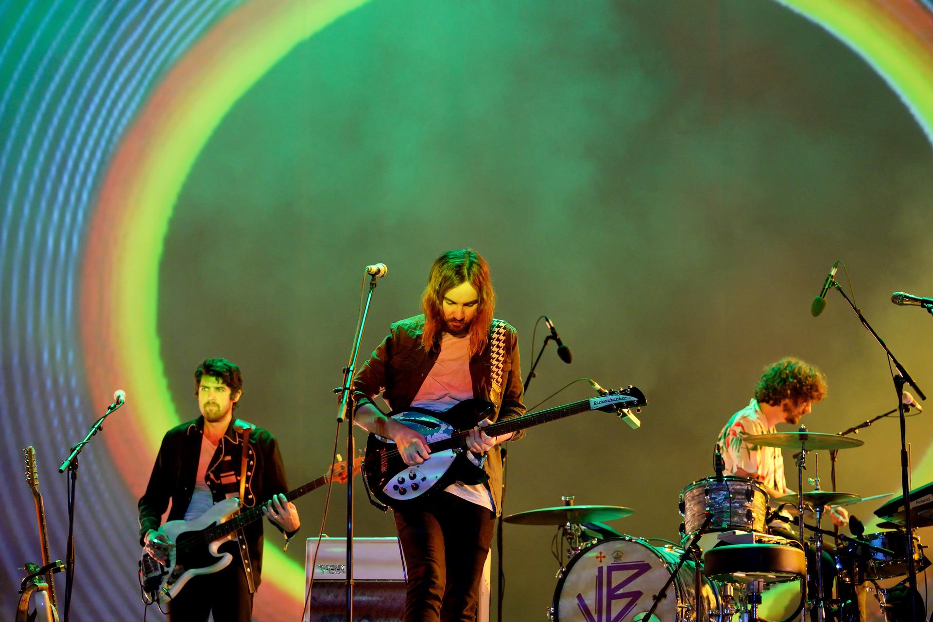 Tame Impala live auf der Bühne: Kevin Parker mit Rickenbacker-Gitarre vor einer Lichtprojektion in Regenbogenfarben